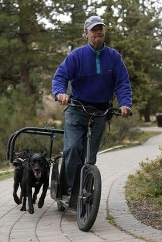Mark Schuette riding one of his own dog-powered scooters on a street in Bend, Oregon.